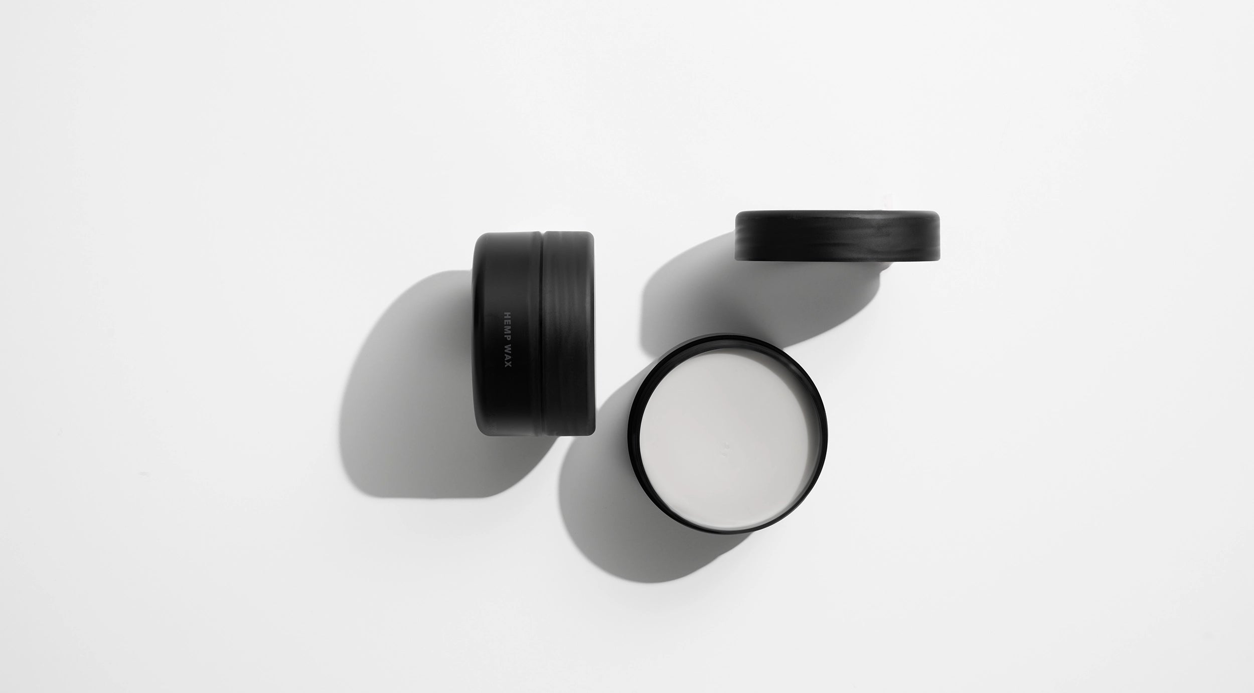 Kreativt opstillet produktbillede af to Hemp Wax fra Black Xclusive. Vokskrukker set oppefra og holdt i sort / hvid.