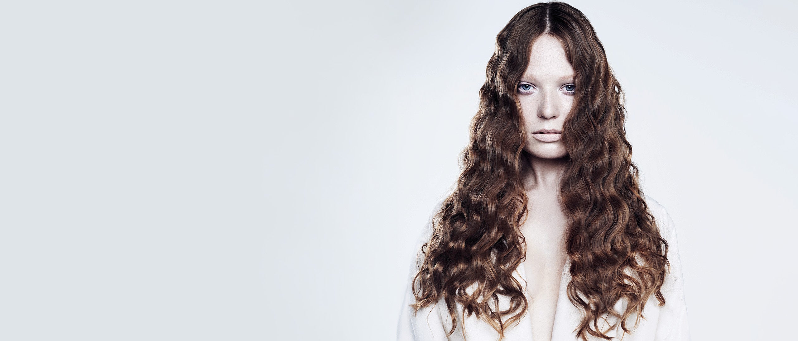 Kvinde med langt, bølget mørkebrunt hår mod lys baggrund.