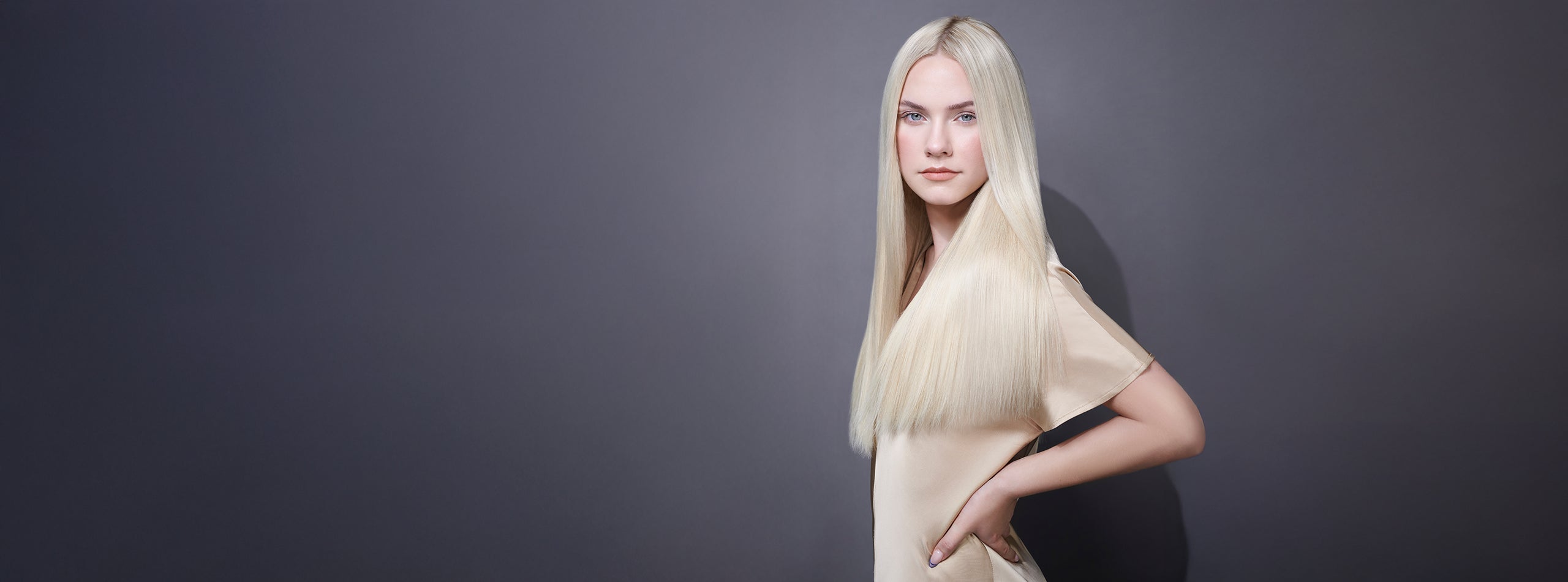 Kvinde med langt, glansfuldt platinblond hår mod grå baggrund.