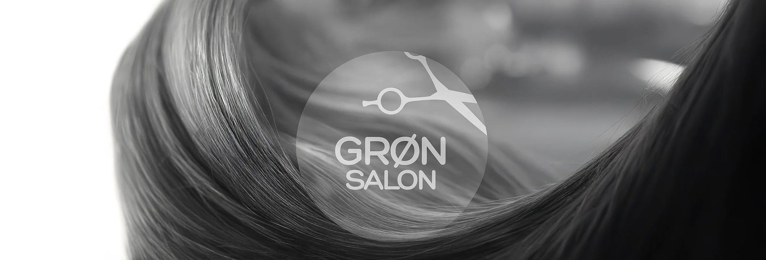 I forgrunden ses IdHAIRs logo for Godkendt til Grøn Salon. I baggrunden ses sort hår på hvid baggrund