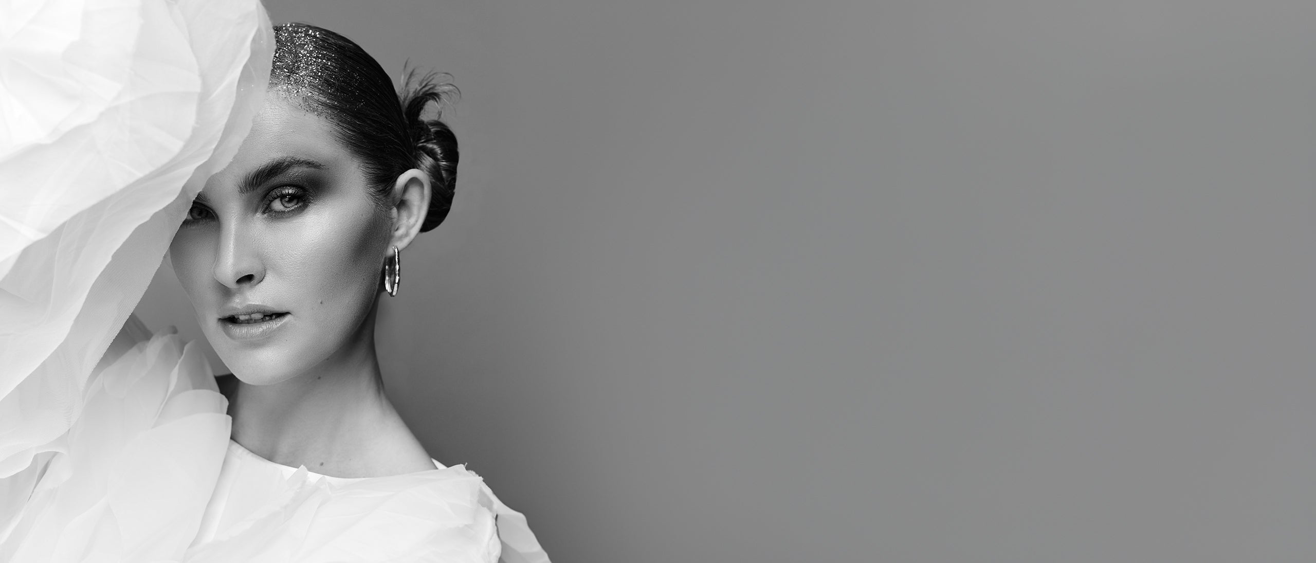 Sort/hvidt billede af kvinde med stramt opsat hår og dramatisk styling i sort-hvid æstetik.