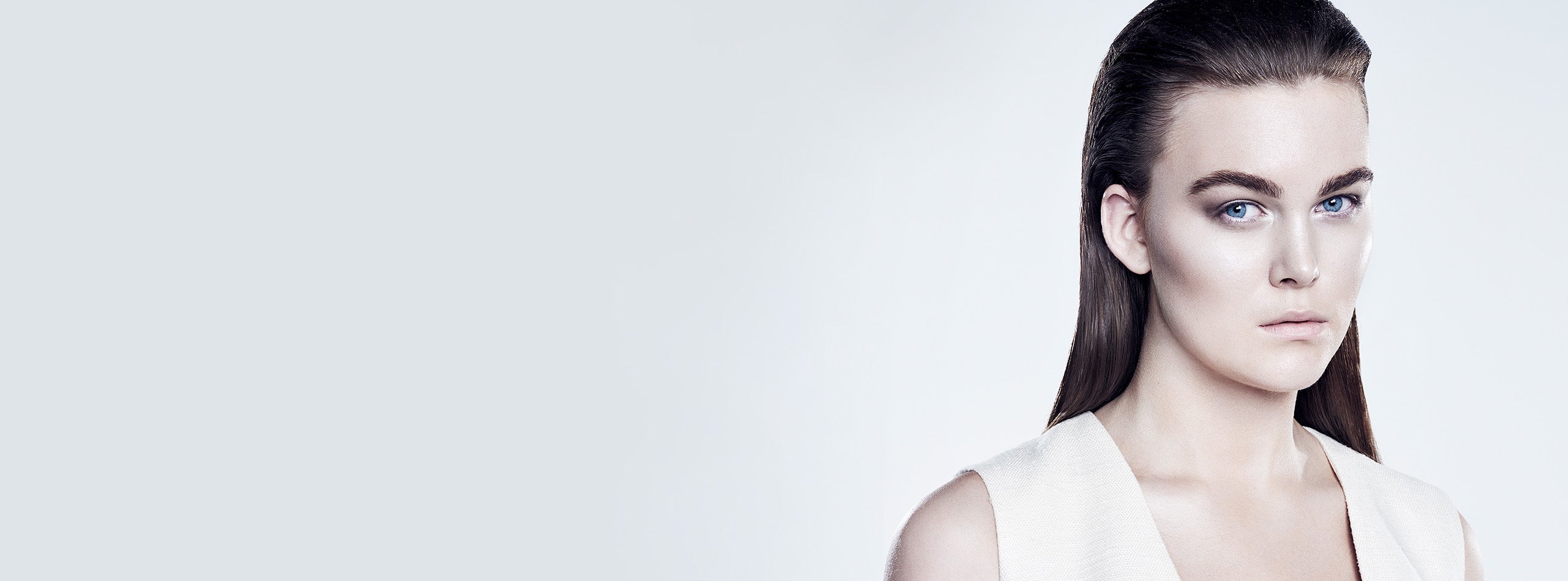 Kvinde med glansfuldt, tilbageredt mørkebrunt hår og markerede bryn mod lys baggrund.