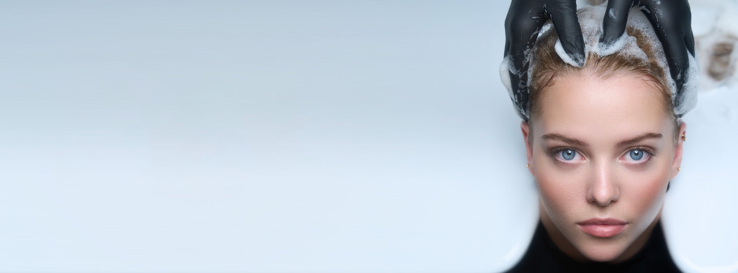 Kvinde får hårvask med IdHAIR produkt, skum masseres ind i håret af frisør med handsker.