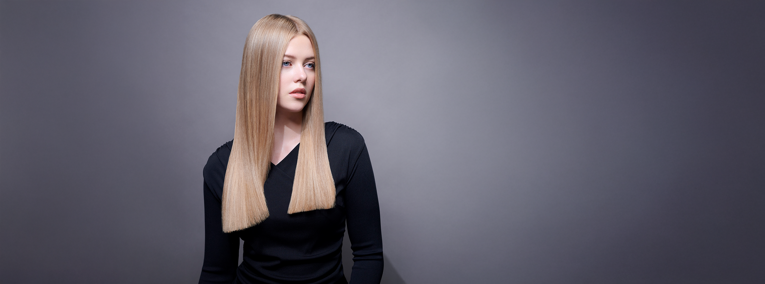 Kvinde med langt, glansfuldt mørkeblond hår mod grå baggrund.