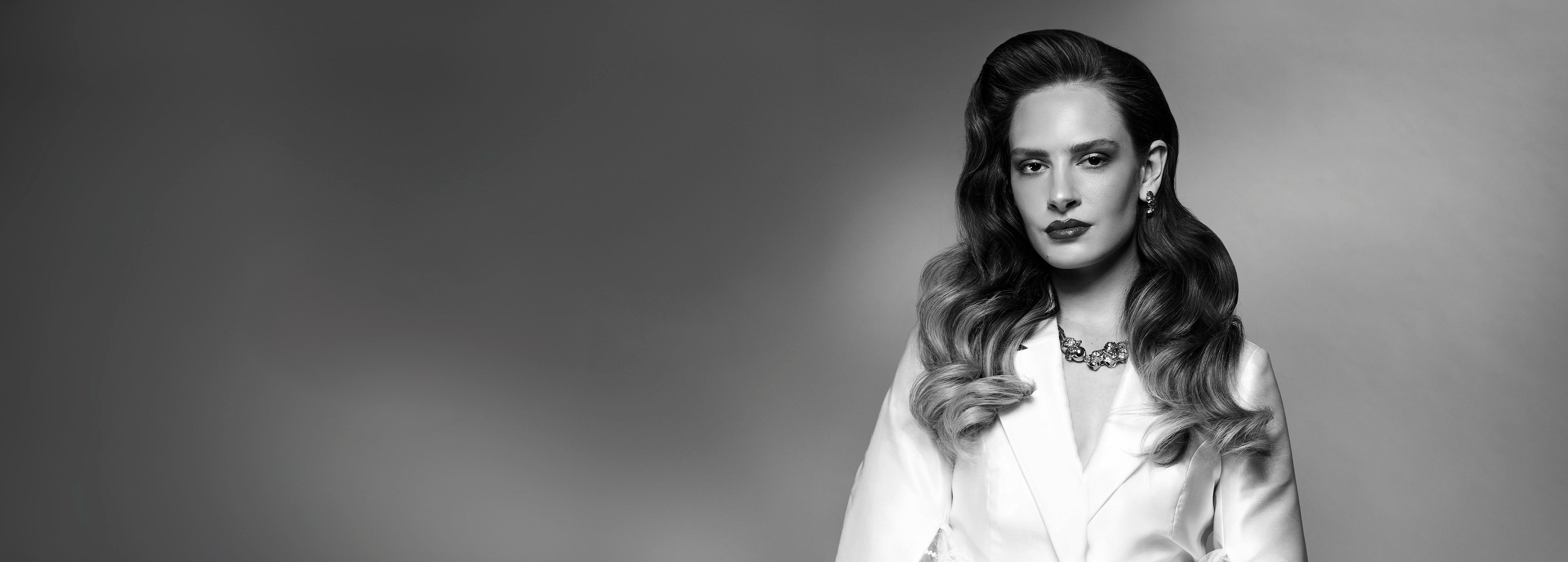 Sort/hvid-billede af kvinde med glansfuldt, bølget hår i klassisk Hollywood-stil mod grå baggrund.